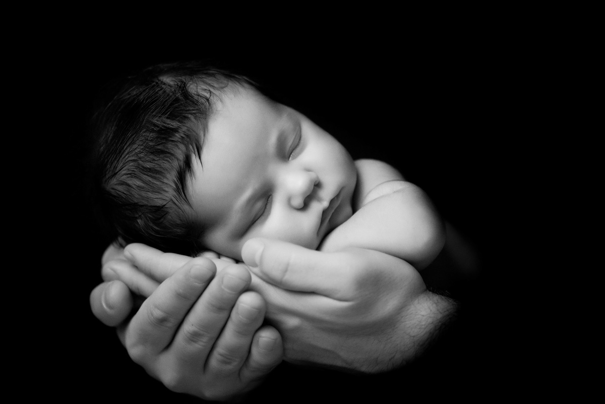 Father's love. Little newborn baby sleeping in Dad 's hands. Close-up on a black background
