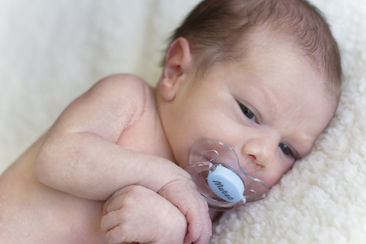 Beautiful newborn baby with blue pacifier, lying on a blanket and looking peacefully