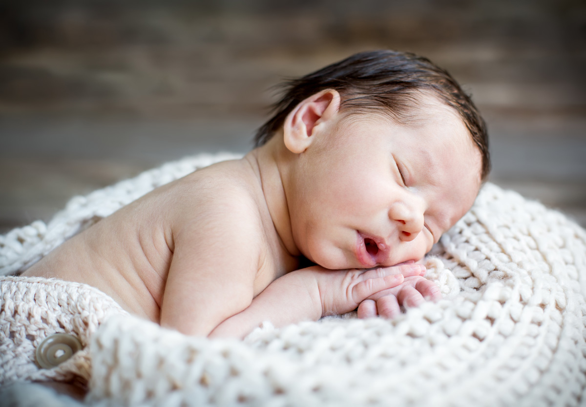 Sleeping newborn baby with dark hair and lanugo.