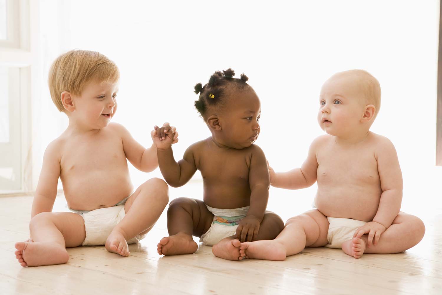 Three babies sitting indoors holding hands